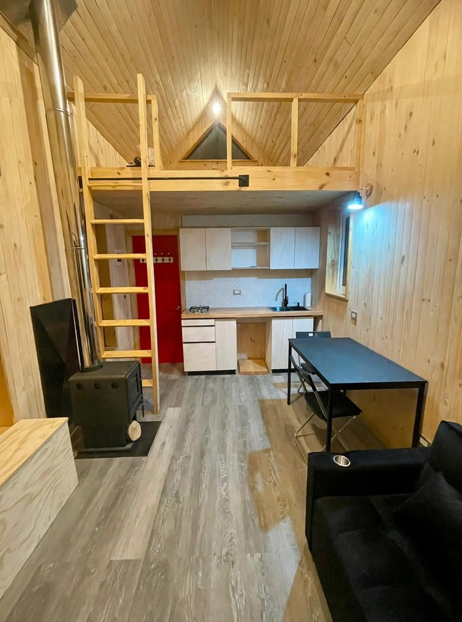 Interior de cabaña Modus Patagonia: entrepiso con escalera de madera, cocina y estufa a leña